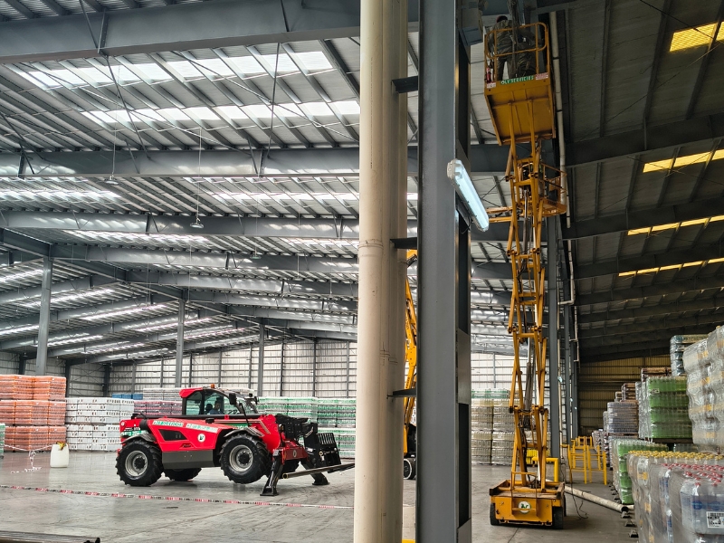 Plataformas elevadoras operando en depósito logístico con racks de almacenamiento - LV Servicios